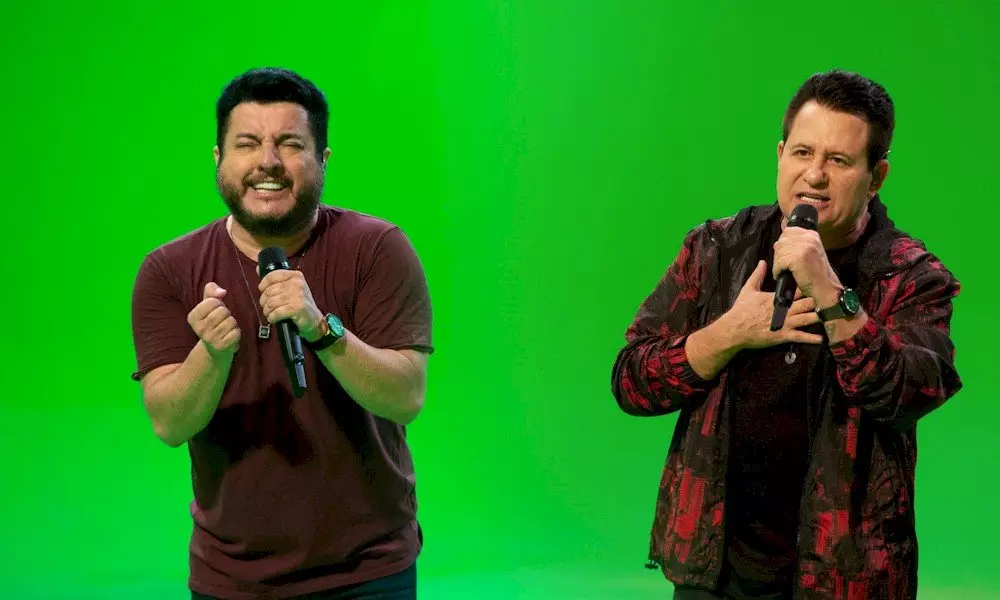 Bruno e Marrone cantando com microfones diante de um fundo verde